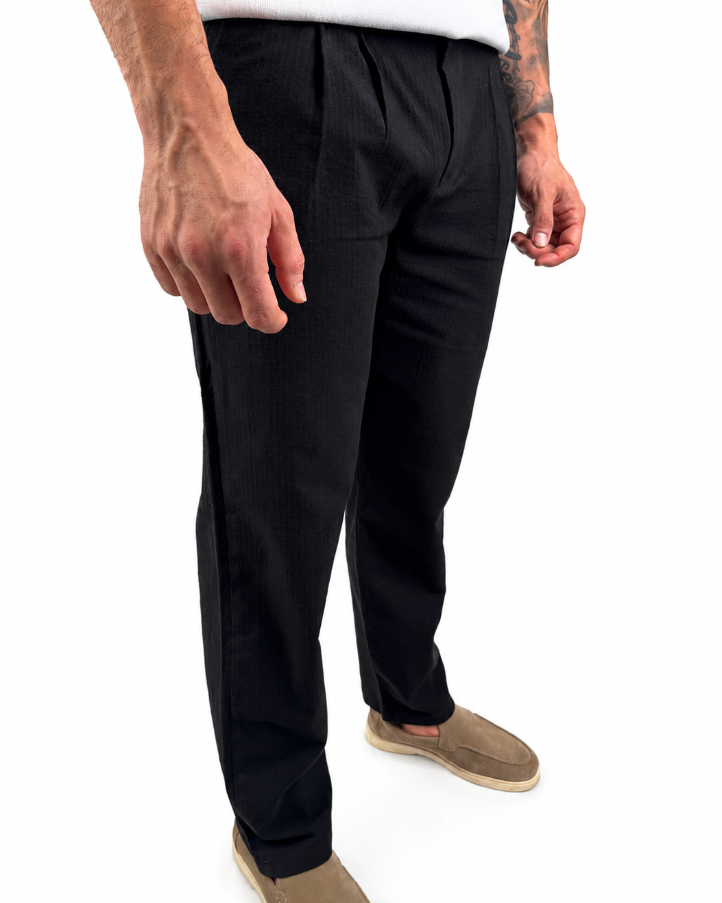A person wearing black trousers with a white shirt and tan slip-on shoes, shown from the waist down against a plain white background.