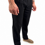 A person wearing black trousers with a white shirt and tan slip-on shoes, shown from the waist down against a plain white background.