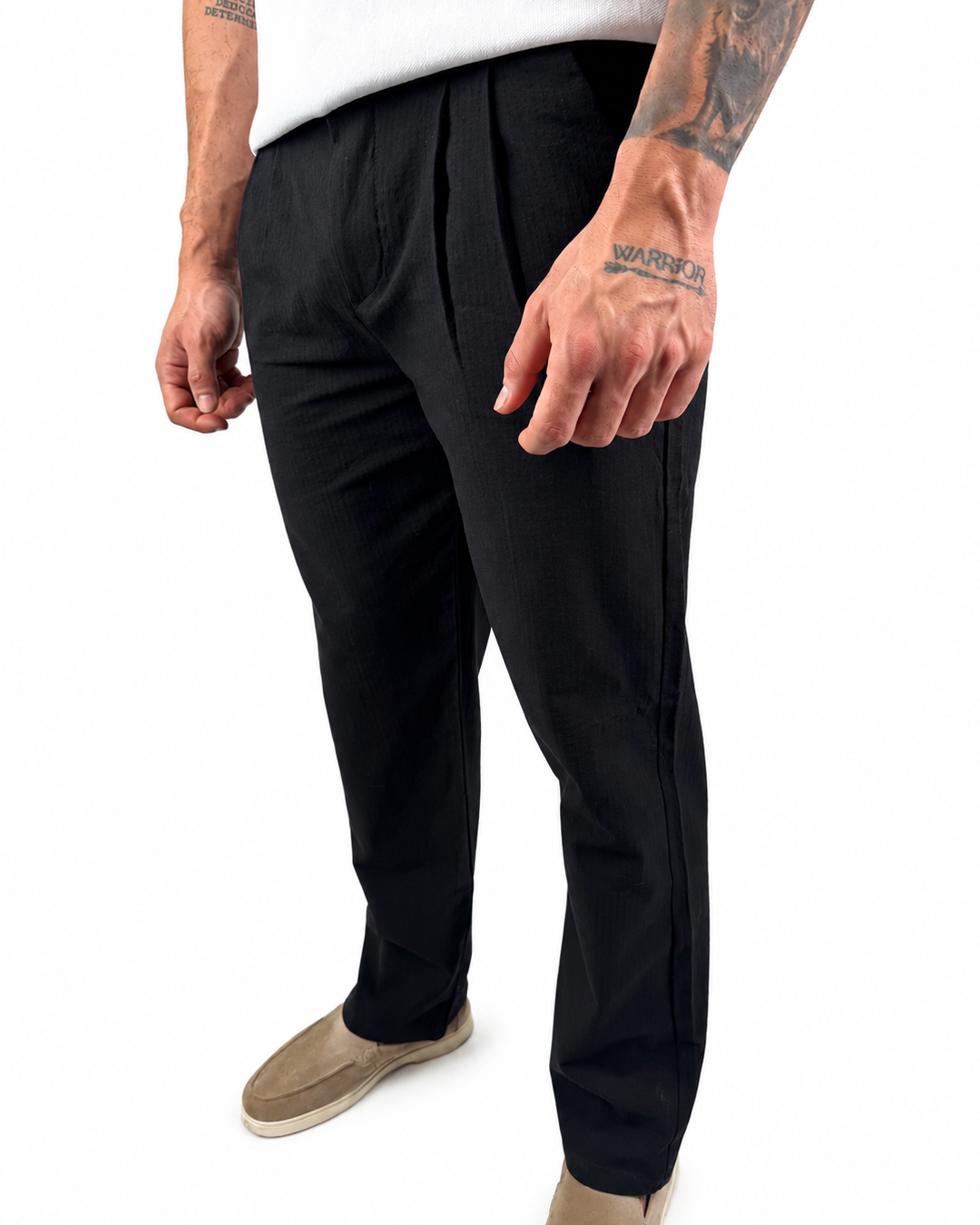 A man wearing black slim-fit trousers, styled with a white t-shirt and beige slip-on shoes, shown from the waist down against a white background.