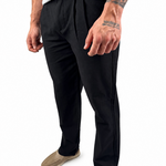 A man wearing black slim-fit trousers, styled with a white t-shirt and beige slip-on shoes, shown from the waist down against a white background.