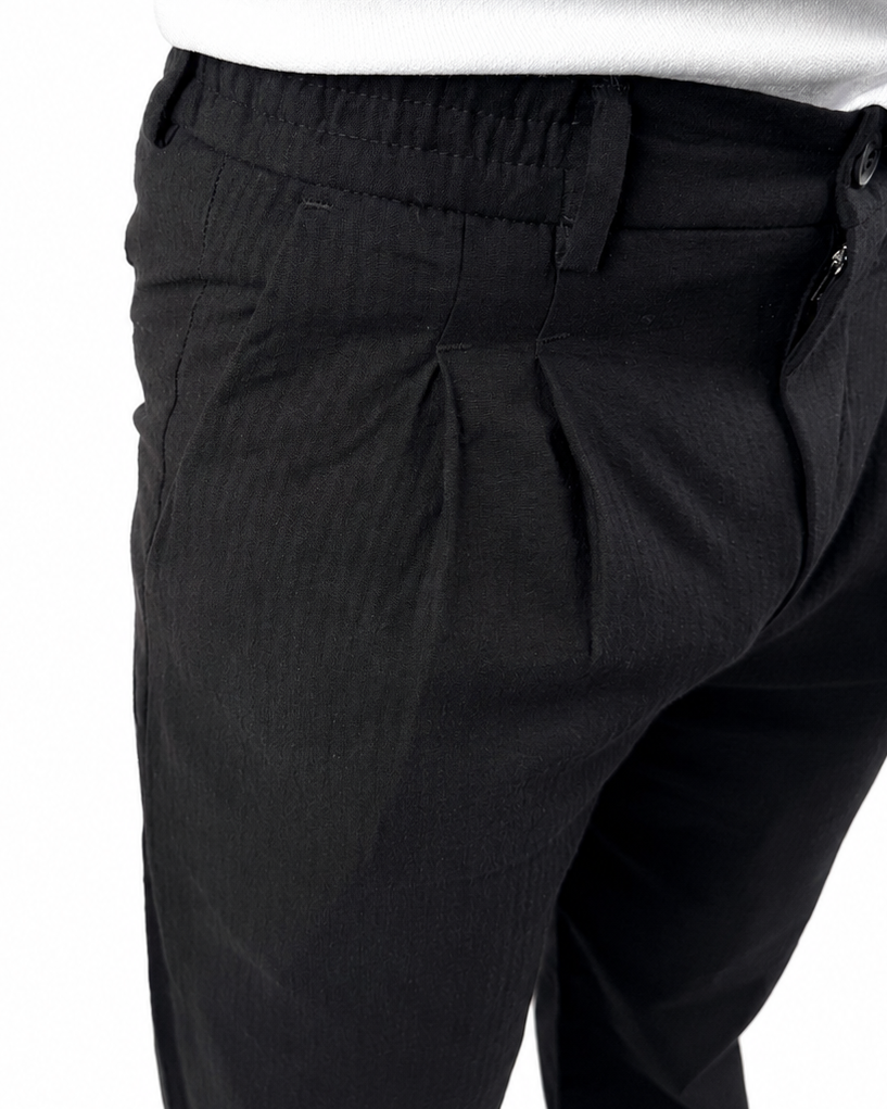 Close-up of a person wearing black pleated trousers and a white shirt, cropped from the chest down against a plain white background.