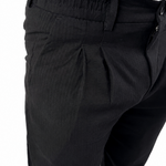 Close-up of a person wearing black pleated trousers and a white shirt, cropped from the chest down against a plain white background.