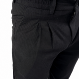 Close-up of a person wearing black pleated trousers and a white shirt, cropped from the chest down against a plain white background.