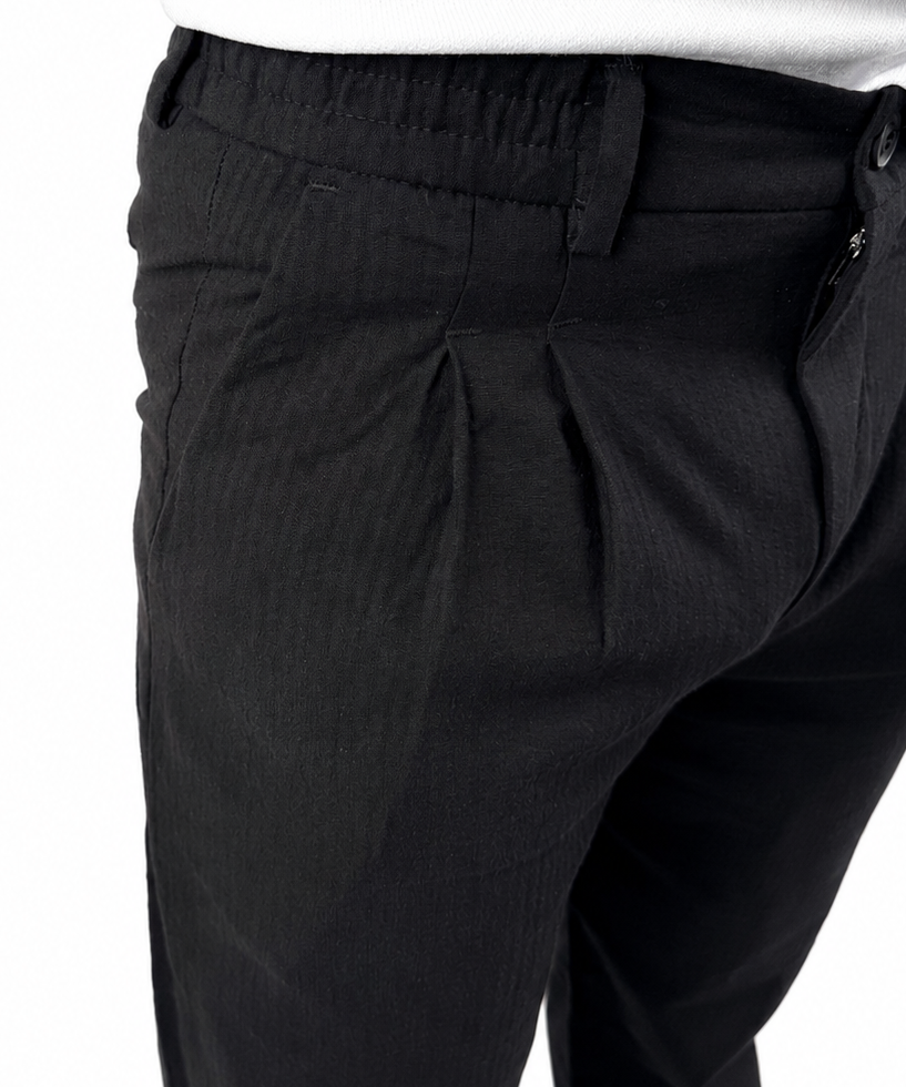 Close-up of a person wearing black pleated trousers and a white shirt, cropped from the chest down against a plain white background.