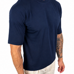 A man wearing a navy blue short-sleeve crewneck t-shirt and off-white pants, shown from the neck down against a plain white background.