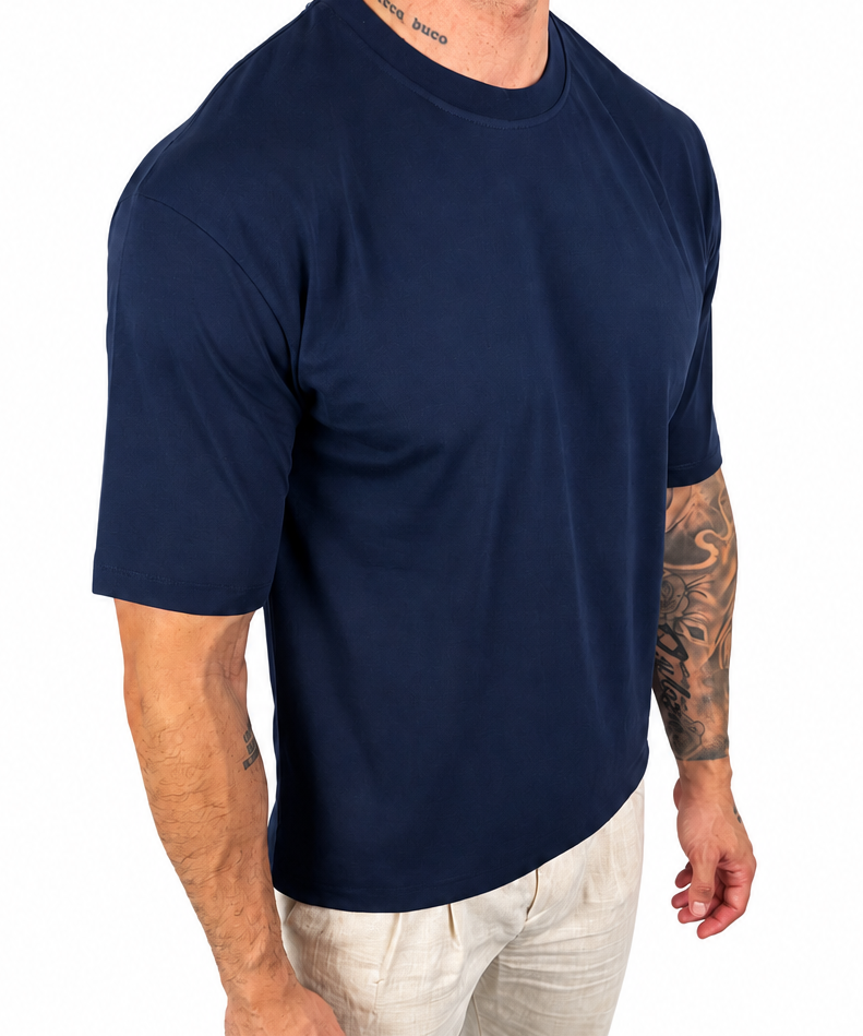 A man wearing a navy blue short-sleeve crewneck t-shirt and off-white pants, shown from the neck down against a plain white background.