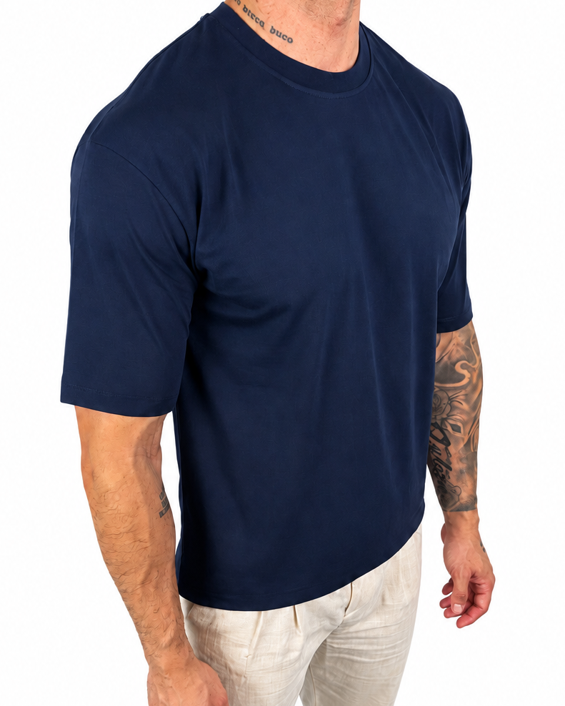 A man wearing a navy blue short-sleeve crewneck t-shirt and off-white pants, shown from the neck down against a plain white background.