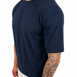 A man wearing a navy blue short-sleeve crewneck t-shirt and off-white pants, shown from a side profile against a solid white background.