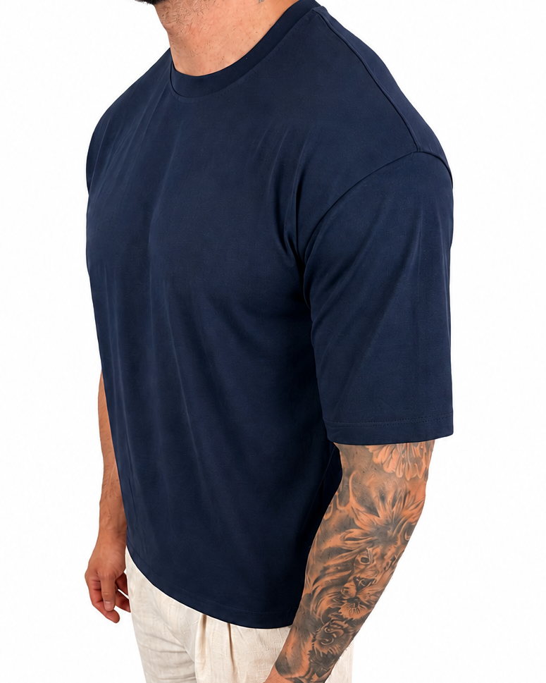 A man wearing a navy blue short-sleeve crewneck t-shirt and off-white pants, shown from a side profile against a solid white background.