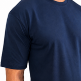A man wearing a navy blue short-sleeve crewneck t-shirt and off-white pants, shown from the neck down against a plain white background.