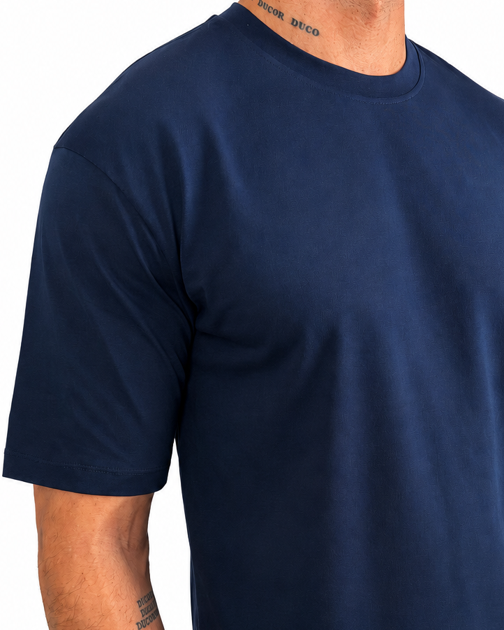 A man wearing a navy blue short-sleeve crewneck t-shirt and off-white pants, shown from the neck down against a plain white background.