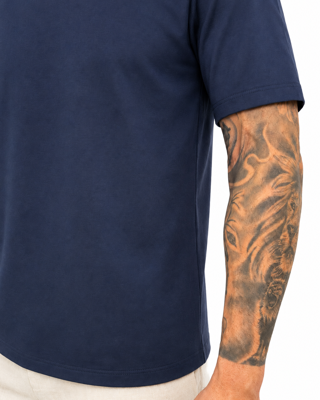 A close-up of a person wearing a navy blue short-sleeve t-shirt and off-white trousers, showing a detailed tattoo on the arm.