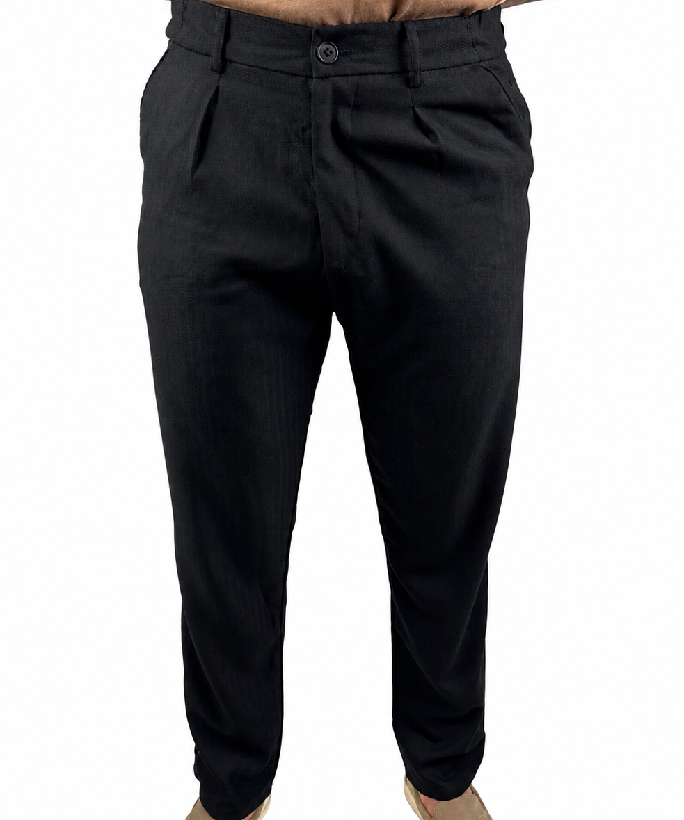 Black slim-fit trousers shown on a model from the waist down, paired with a tan shirt and beige slip-on shoes against a plain white background.