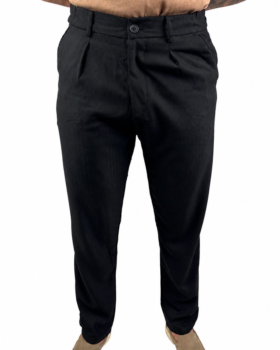 Black slim-fit trousers shown on a model from the waist down, paired with a tan shirt and beige slip-on shoes against a plain white background.