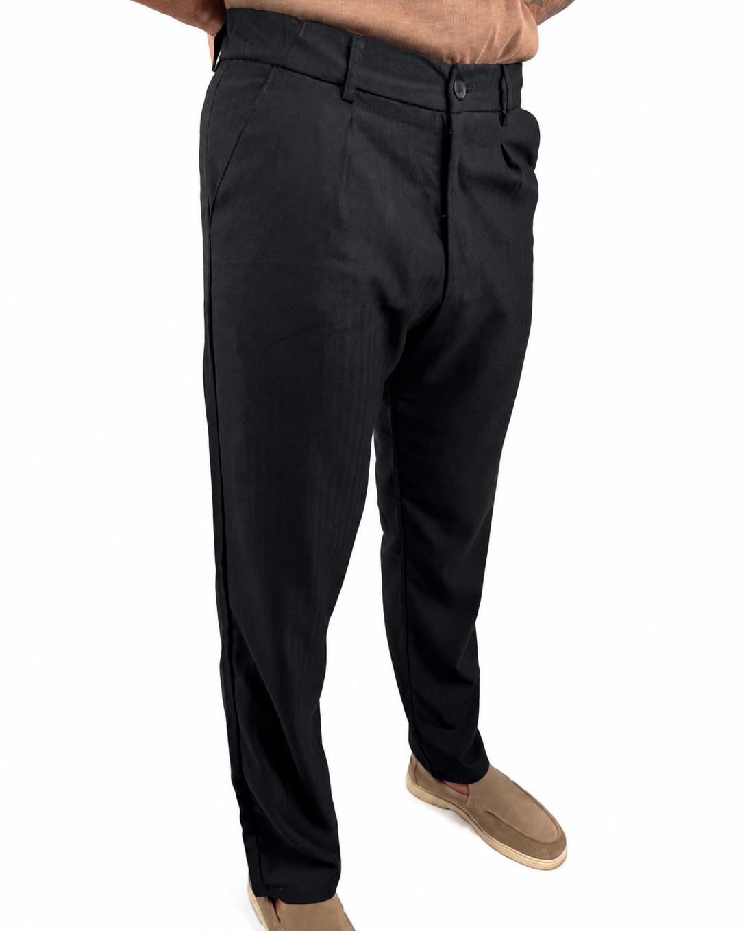 A person wearing black slim-fit dress pants with tan slip-on shoes, shown from the waist down against a plain white background.