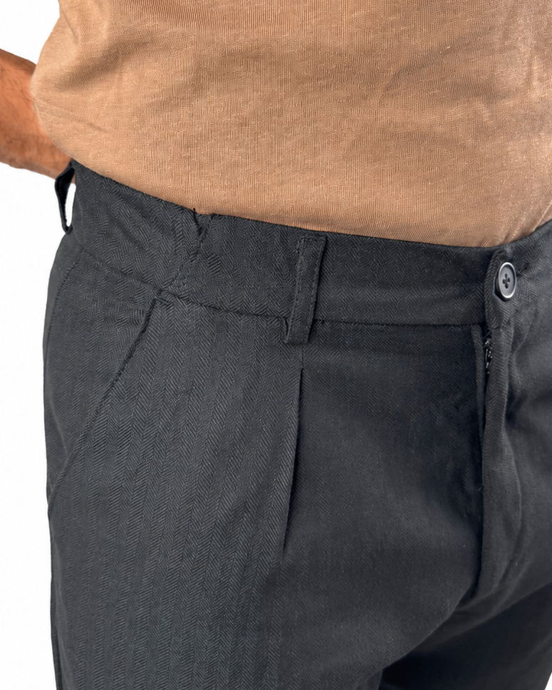 Close-up of a person wearing dark charcoal gray trousers and a tan knit top against a plain white background.