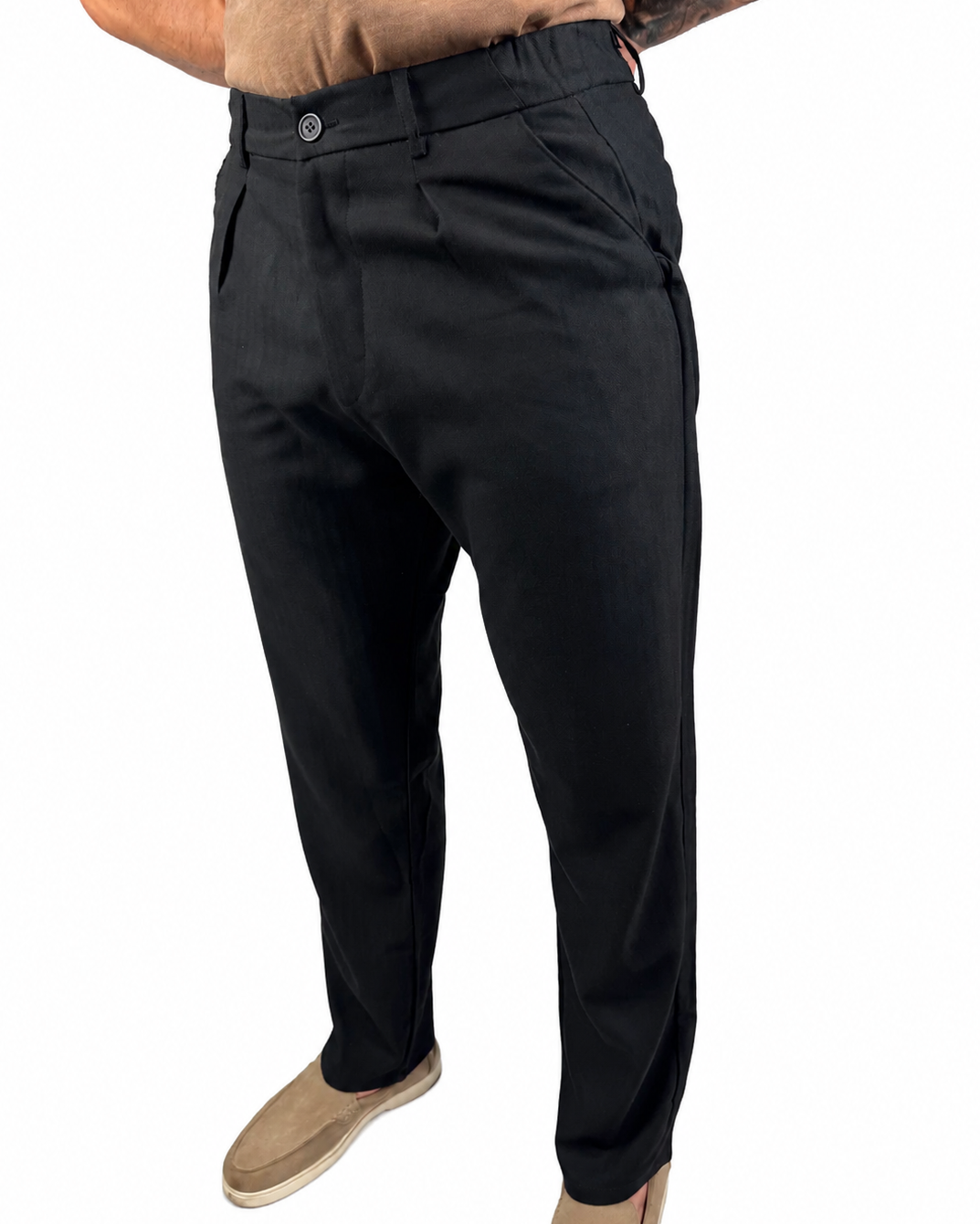 A person wearing black slim-fit trousers, shown from the waist down against a plain white background. The model is also wearing a tan shirt and tan slip-on shoes.