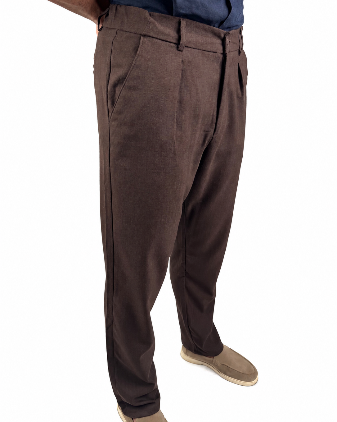 A person wearing dark brown dress pants with a blue shirt and tan shoes, shown from the waist down on a white background.