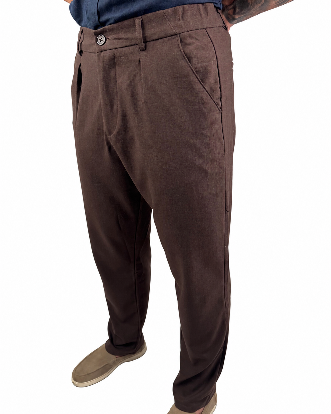 A person wearing dark brown trousers, a navy blue shirt, and tan slip-on shoes, shown from the waist down against a plain white background.