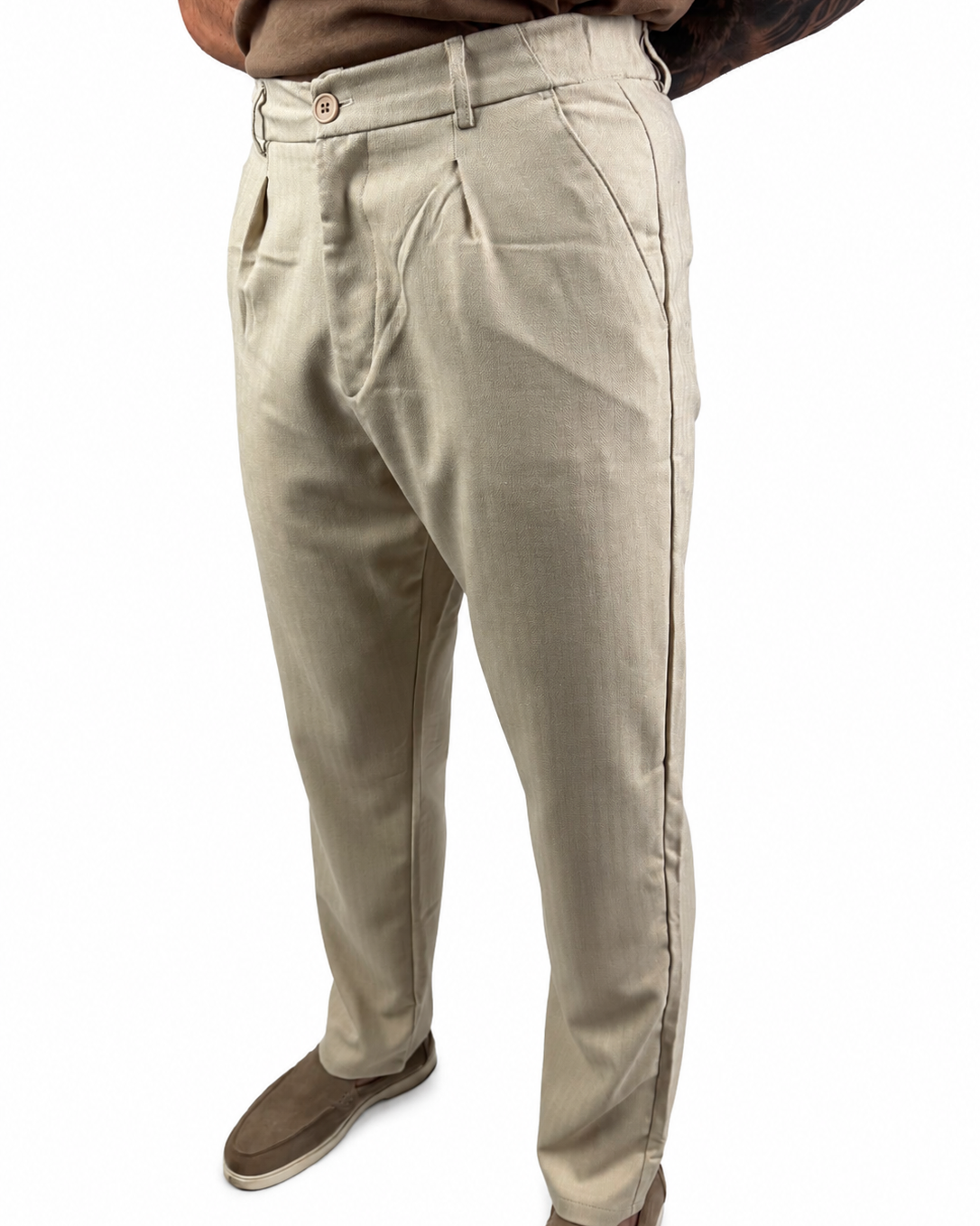 A person wearing light beige chinos or casual trousers, paired with brown suede shoes and a brown shirt, shown from the waist down on a white background.