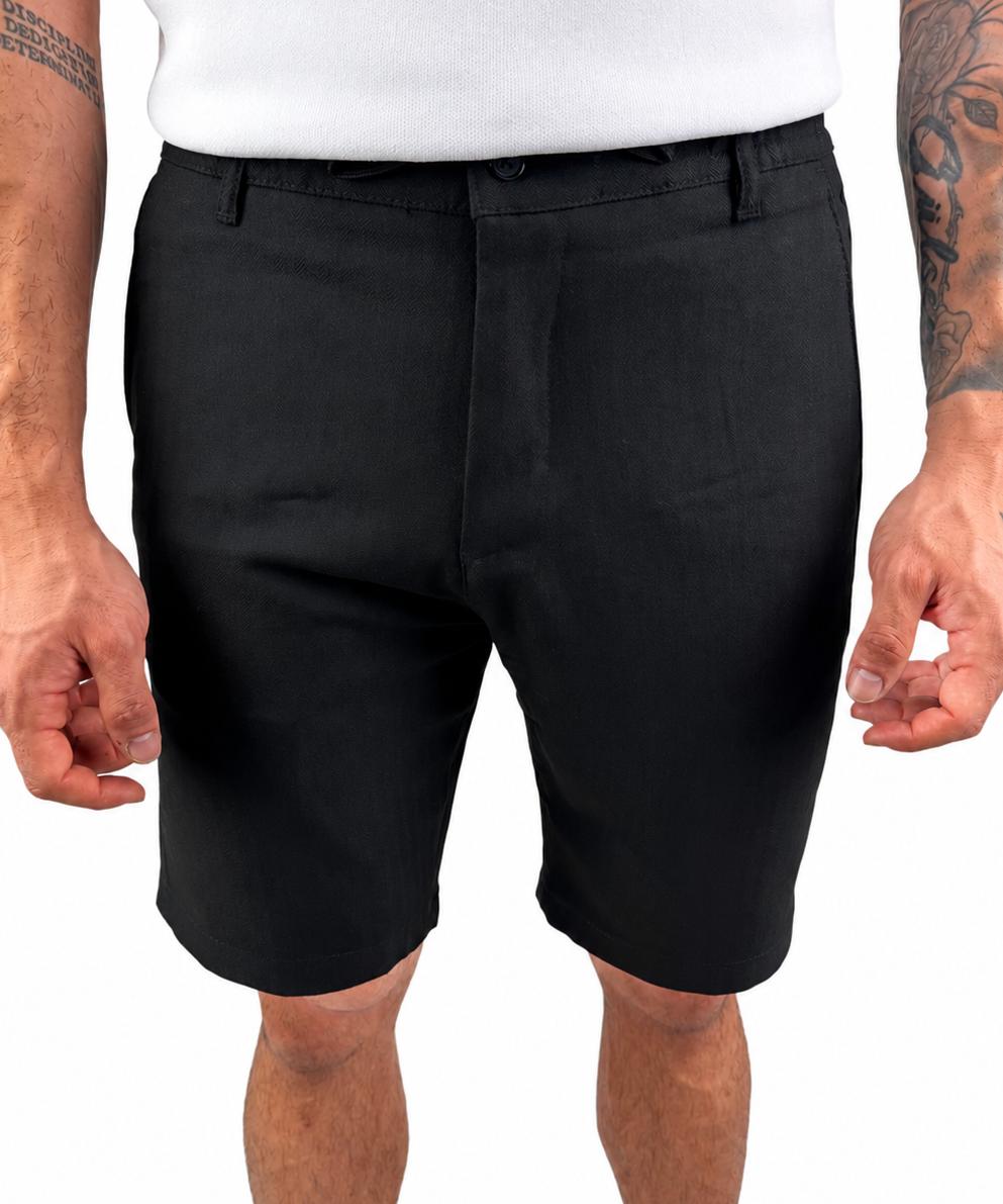 A man wearing black tailored shorts and a white t-shirt, cropped from the chest down, standing against a plain white background.