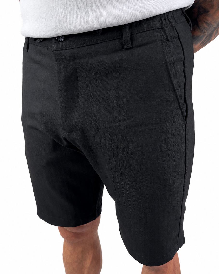 A person wearing black casual shorts with a white top, shown from the waist down against a plain white background.