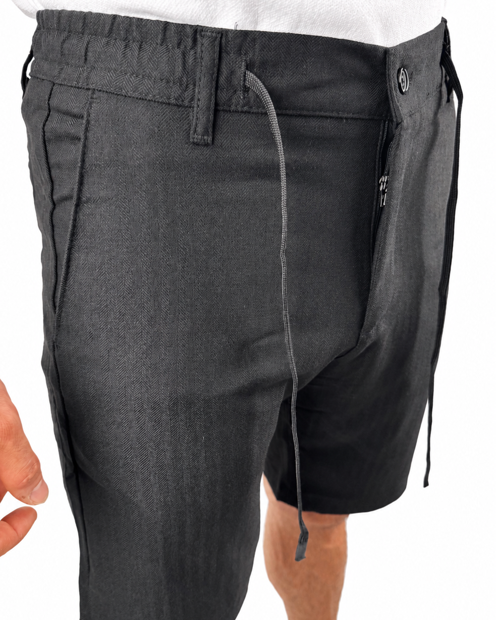 Dark gray drawstring shorts with a unique asymmetrical zipper closure and side pockets, shown on a model against a white background.