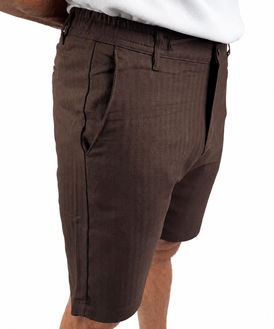 A close-up side view of a person wearing dark brown textured shorts and a white t-shirt, cropped from the waist down against a plain white background.