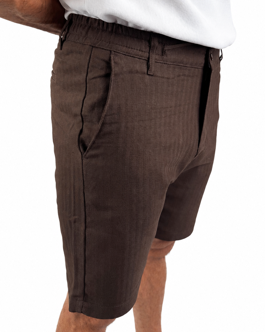 A close-up side view of a person wearing dark brown textured shorts and a white t-shirt, cropped from the waist down against a plain white background.