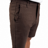 A close-up side view of a person wearing dark brown textured shorts and a white t-shirt, cropped from the waist down against a plain white background.