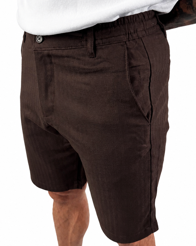 A person wearing dark brown linen shorts and a white tank top, shown from the chest down against a plain white background.