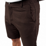 A person wearing dark brown linen shorts and a white tank top, shown from the chest down against a plain white background.