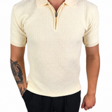 A man wearing a short-sleeve polo shirt with a subtle grid texture in cream or pale yellow, paired with black pants, shown against a plain white background.