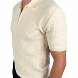 A man wearing a short-sleeve knit polo shirt in cream with a subtle grid texture, paired with black pants, shown from a side profile against a white background.
