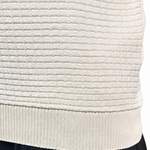 Close-up of a person wearing a cream ribbed knit sweater vest and black pants against a white background.