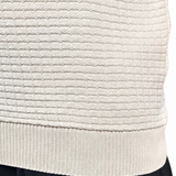 Close-up of a person wearing a cream ribbed knit sweater vest and black pants against a white background.