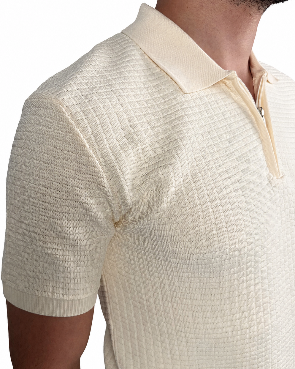 A close-up of a man wearing a cream-colored short-sleeve polo shirt with a basket knit pattern and a polo.