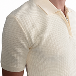 A close-up of a man wearing a cream-colored short-sleeve polo shirt with a basket knit pattern and a polo.