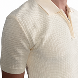 A close-up of a man wearing a cream-colored short-sleeve polo shirt with a basket knit pattern and a polo.