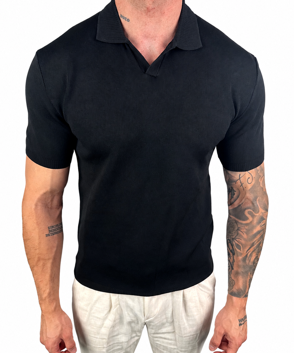 A man wearing a black short-sleeve polo shirt and off-white trousers, shown from the neck down against a plain white background.