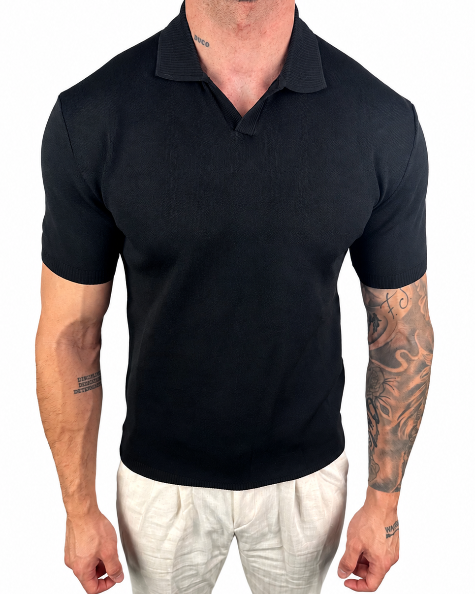 A man wearing a black short-sleeve polo shirt and off-white trousers, shown from the neck down against a plain white background.