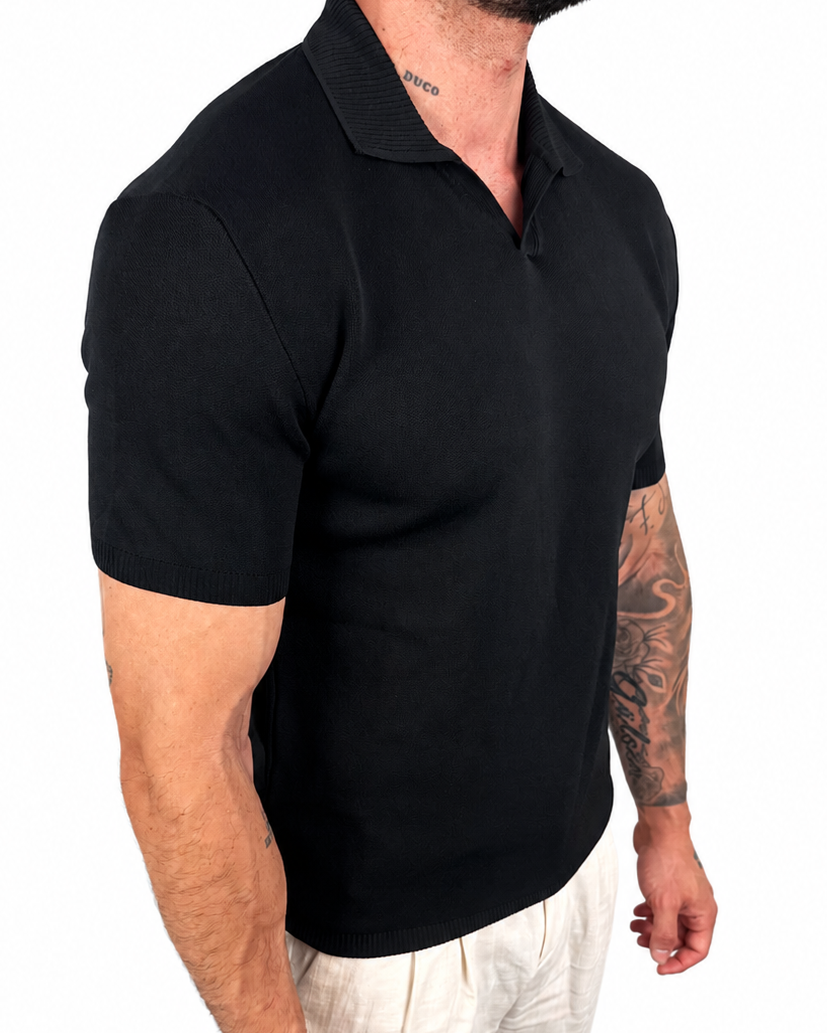 A man wearing a black short-sleeve polo shirt and light beige trousers, shown from the side against a plain white background.