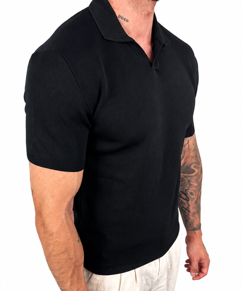 A man wearing a black short-sleeve polo shirt and light beige trousers, shown from the side against a plain white background.