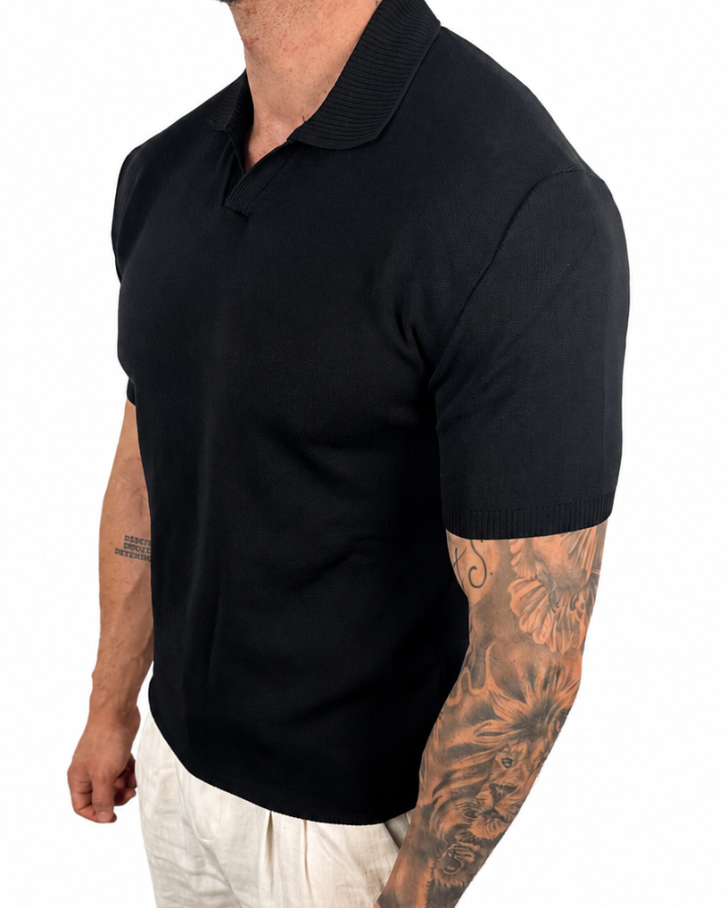 A man wearing a black short-sleeve polo shirt and off-white trousers, shown from the side against a plain white background.