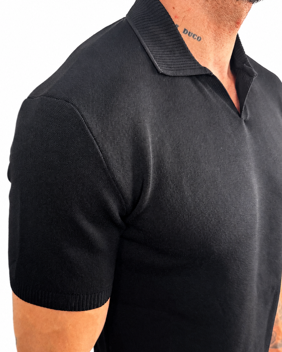 A close-up side view of a man wearing a black short-sleeve knit polo shirt against a plain white background.