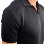 A close-up side view of a man wearing a black short-sleeve knit polo shirt against a plain white background.