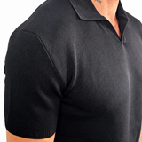 A close-up side view of a man wearing a black short-sleeve knit polo shirt against a plain white background.