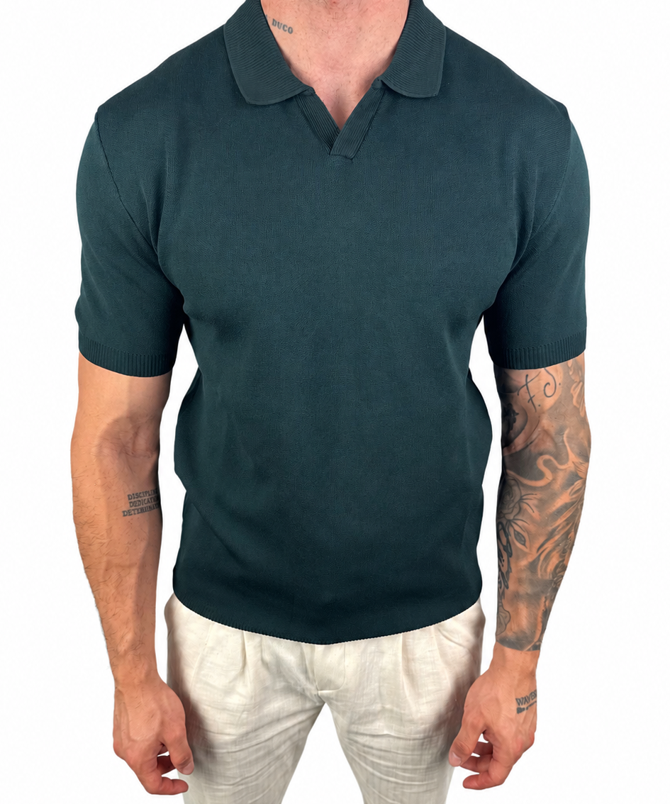 A man wearing a dark teal short-sleeve polo shirt and off-white trousers, shown from the neck down against a plain white background.
