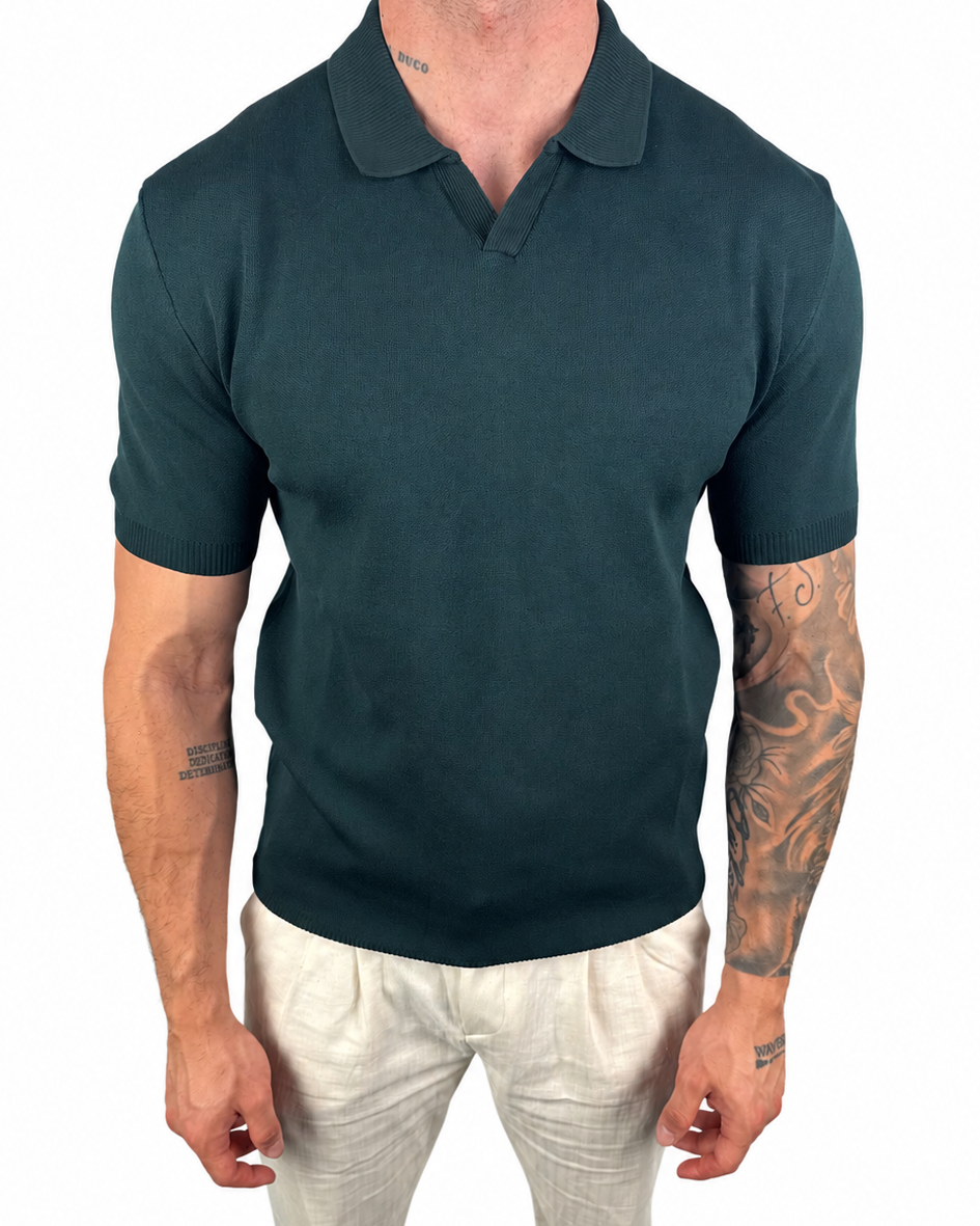 A man wearing a dark teal short-sleeve polo shirt and off-white trousers, shown from the neck down against a plain white background.