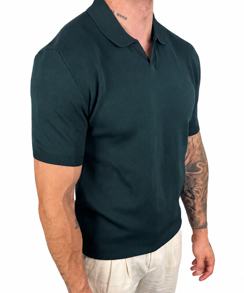 A man wearing a dark green short-sleeve polo shirt and off-white trousers, shown from the neck down against a plain white background.